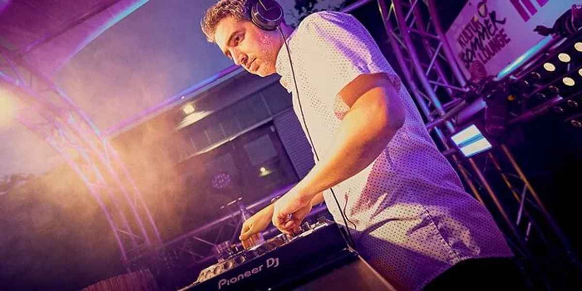 DJ Beatgee legt mit Kopfhörern unter violettem Bühnenlicht auf